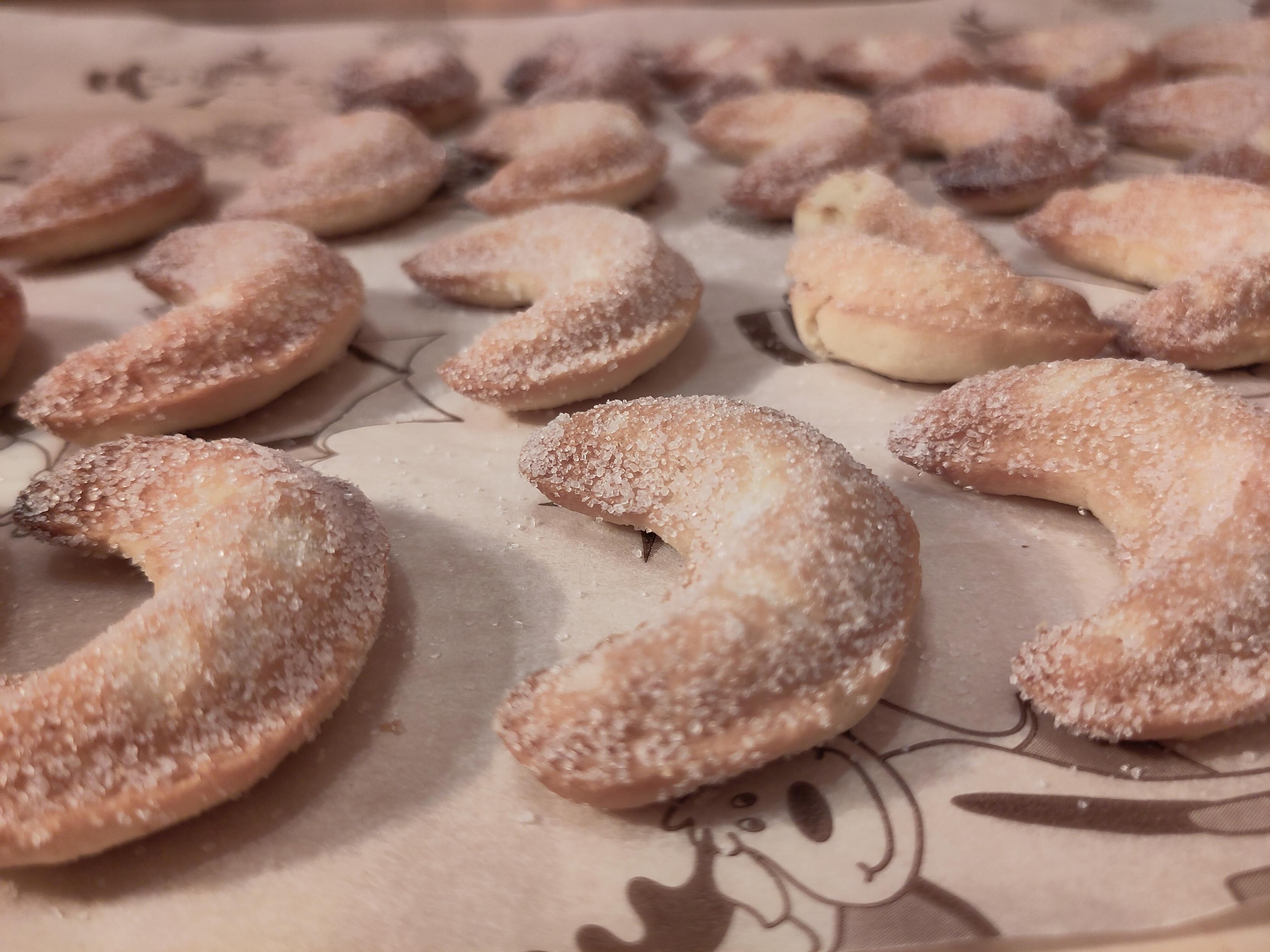 Halbmondförmige Vanille-Kipferl, die in Zucker gewälzt wurden auf Backpapier mit weihnachtlichen Motiven.